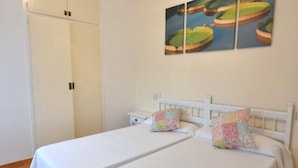A bedroom with two single beds, a white wardrobe, and a wall-mounted painting. - Enjoy your Vacation in this Cozy Apartment in Roses, Costa Brava! Just a few steps from the beach and with all the amenities you need. (Rosas / Roses)