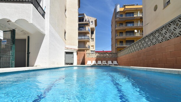 A swimming pool with clear blue water, surrounded by white walls and a brick wall on one side. - Enjoy your Vacation in this Cozy Apartment in Roses, Costa Brava! Just a few steps from the beach and with all the amenities you need. (Rosas / Roses)