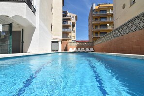 Una piscina con agua cristalina azul, rodeada de muros blancos y una pared de ladrillo en un lateral.
