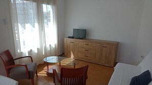 A living room with a glass-top table, wooden cabinet, and a white sofa. - Enjoy your Vacation in this Cozy Apartment in Roses, Costa Brava! Just a few steps from the beach and with all the amenities you need. (Rosas / Roses)