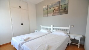 Una habitación de hotel con dos camas individuales, un armario blanco y una mesita de noche pequeña.