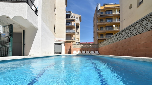 Una piscina con agua cristalina azul, rodeada de muros blancos y una pared de ladrillo en un lateral.