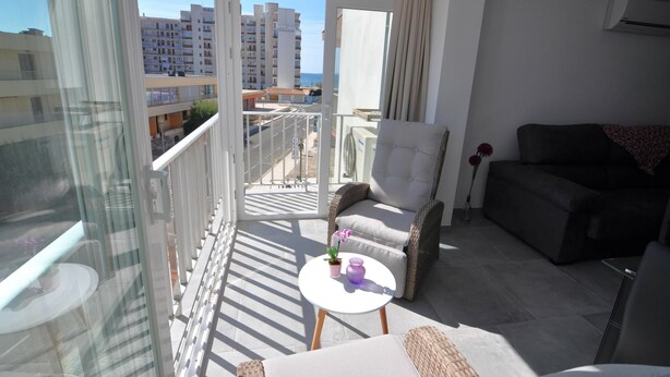 A balcony with a white chair, a dark sofa, and a small table with a vase and a plant.