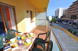 Un balcon avec une table dressée pour le repas, des chaises et une fenêtre donnant sur la rue et les bâtiments.