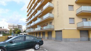 Um edifício com várias andares, varandas e um carro estacionado em frente.