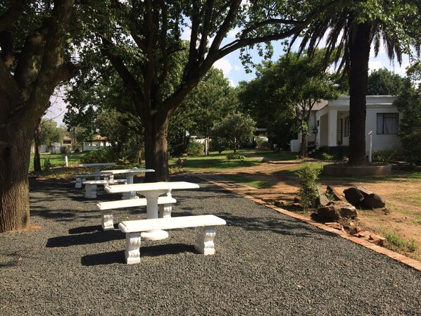 A park with white picnic tables and a white building in the background.