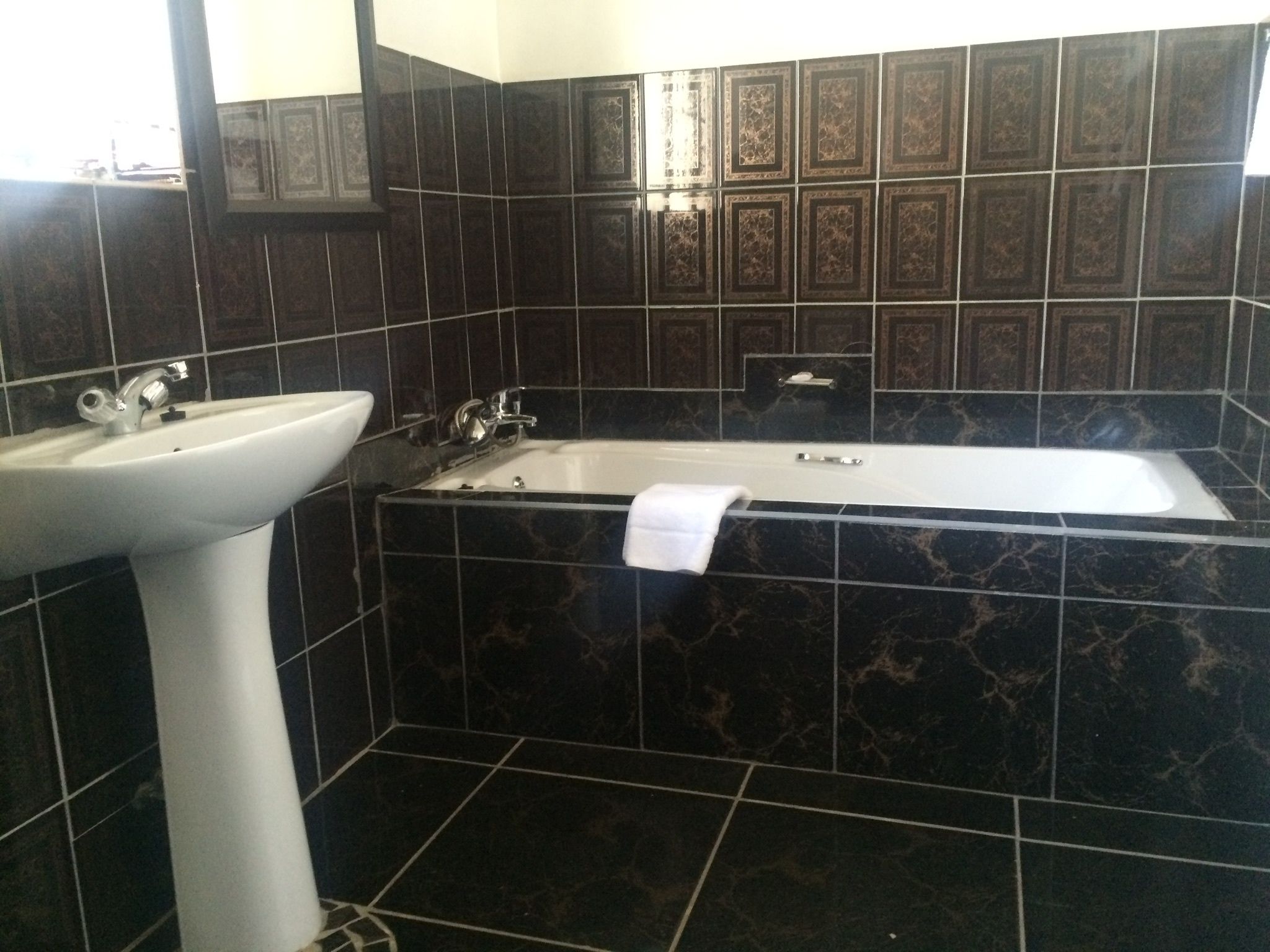 A bathroom with a white sink, a bathtub, and dark tiled walls.