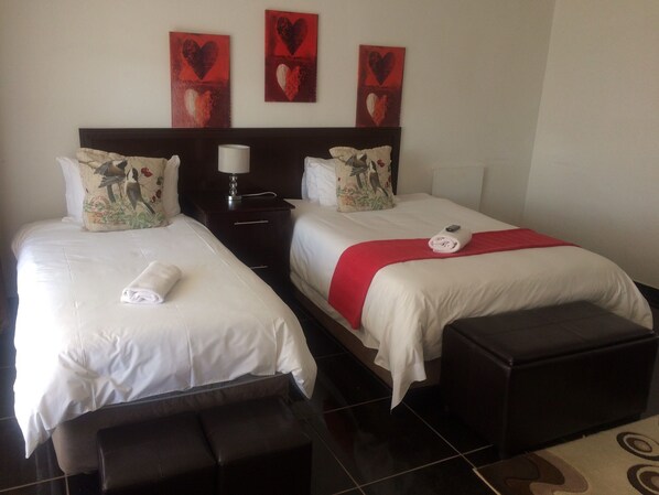 A hotel room with two beds, a nightstand, a lamp, and a red heart-themed artwork on the wall.