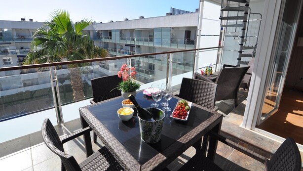 A balcony with a table set for dining, a potted plant, and a view of the cityscape.