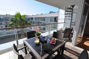 Een balkon met een eettafel, een bloempot en uitzicht op de stad.