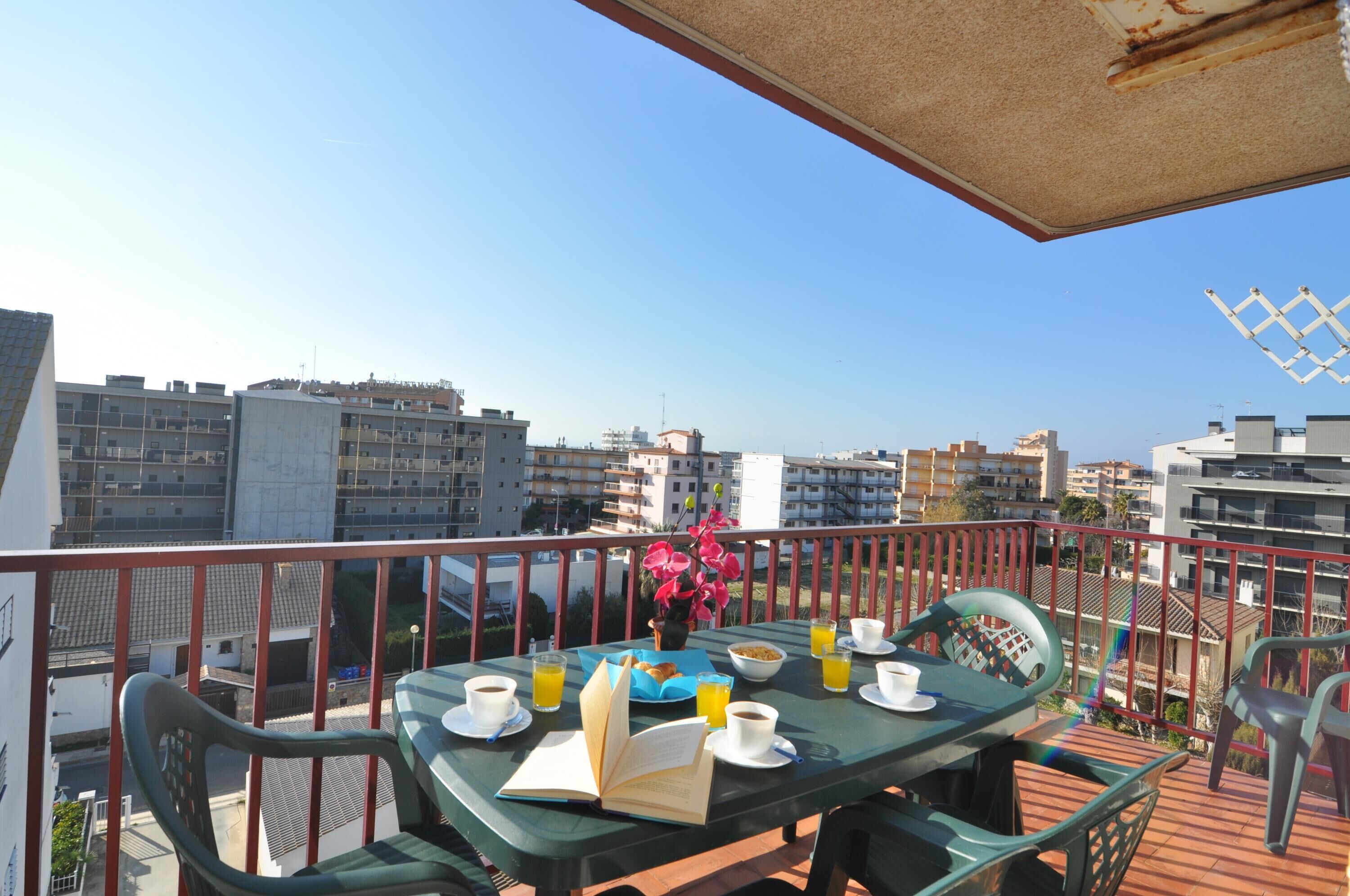 Un balcon avec une table préparée pour le petit-déjeuner, comprenant un livre, des tasses à café et du jus d’orange.