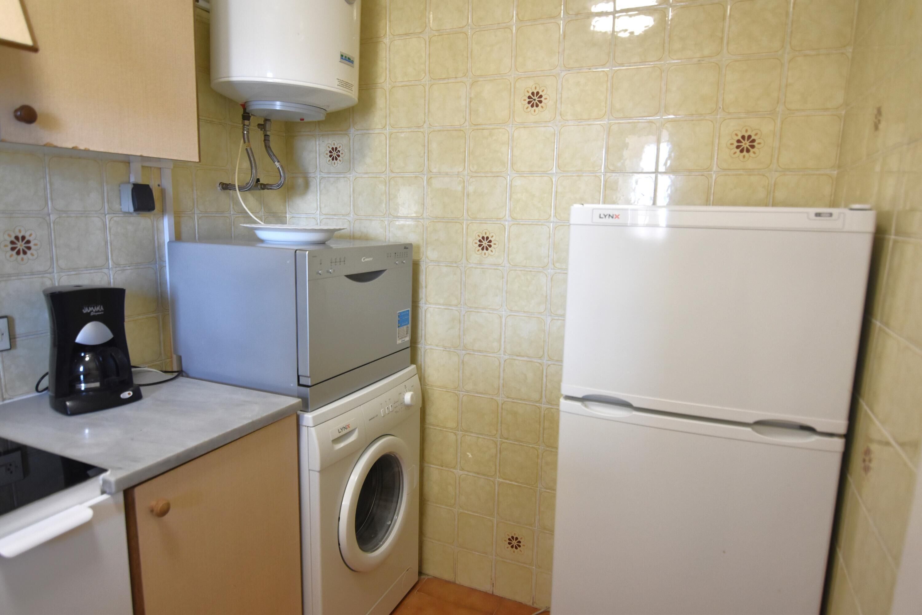 Eine kleine Küche mit Waschmaschine, Kaffeemaschine und Kühlschrank.
