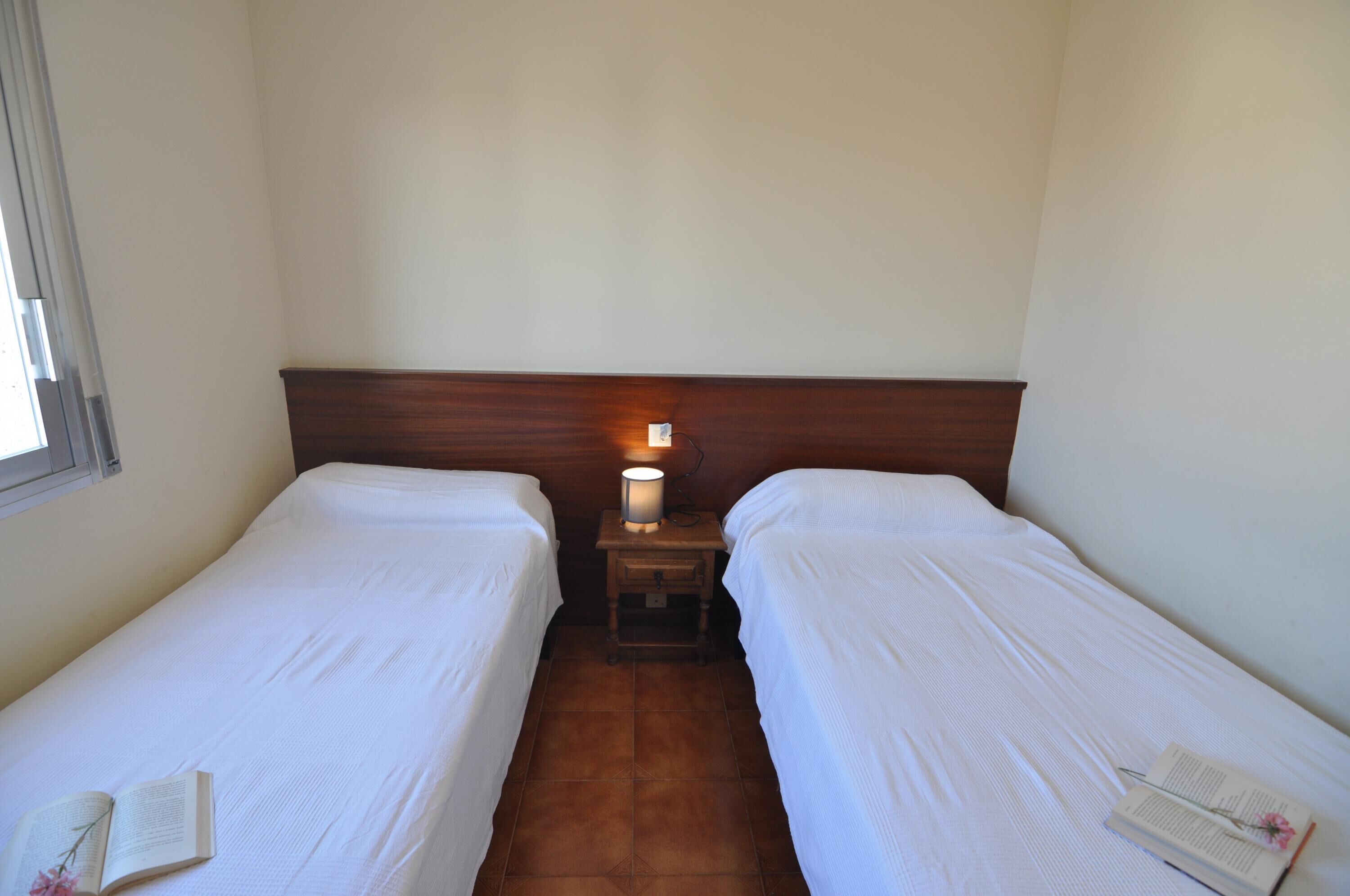 Habitación doble con dos camas individuales, una mesita de noche con lámpara y ventana.