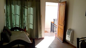 Ein Schlafzimmer mit Bett, Holzstuhl, kleinem Tisch, Heizkörper und Blick auf einen Balkon.