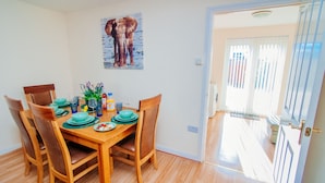 A dining area with a wooden table set for four, surrounded by chairs. A painting of elephants hangs on the wall. - Harris House (Doncaster)