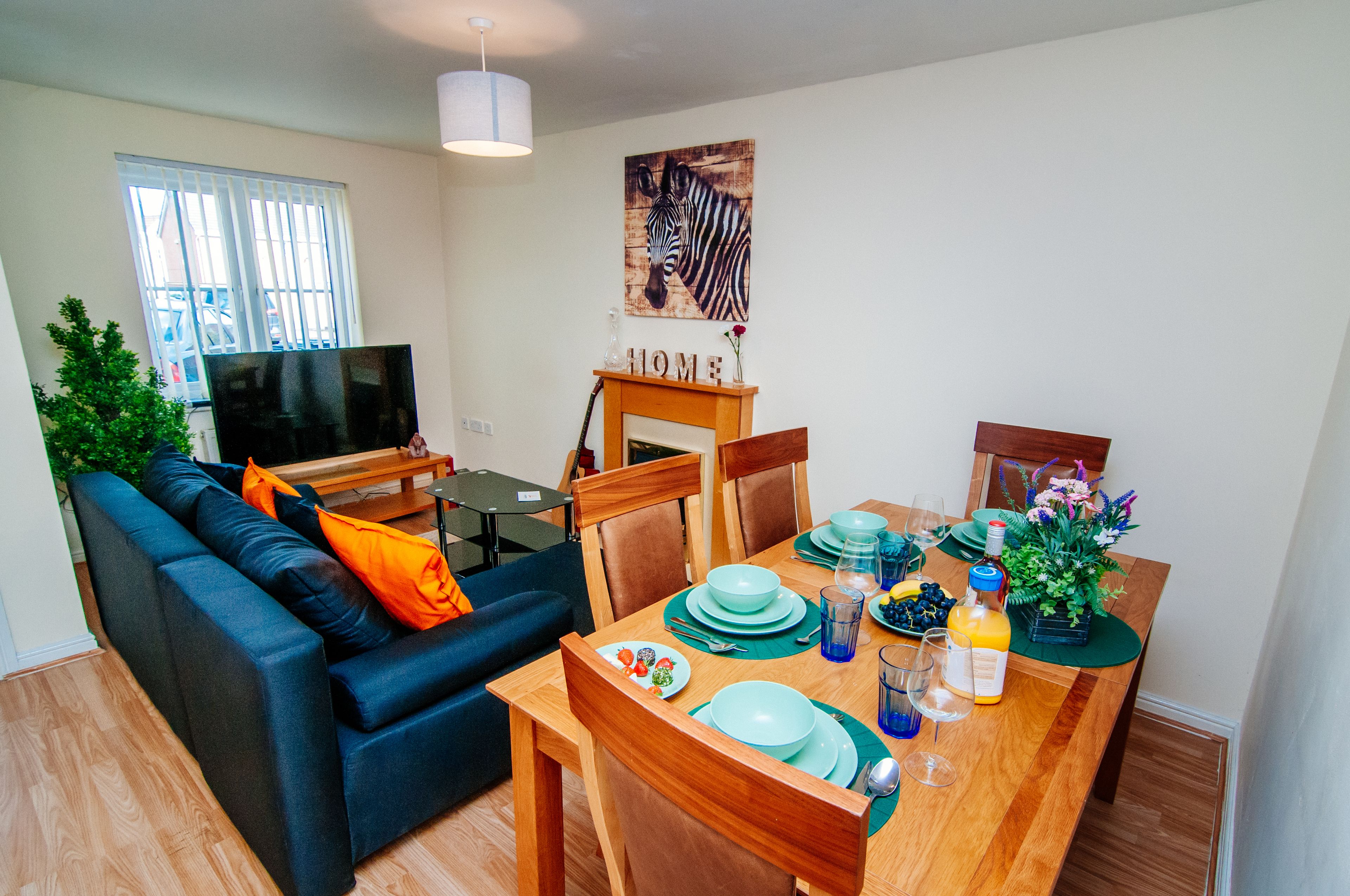 A modern living room with a sofa, TV, dining table set with plates, glasses, and a vase of flowers.