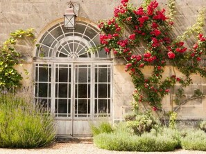 Un edificio histórico con un gran ventanal arqueado, un farol encima y flores rojas vibrantes trepando por la pared.