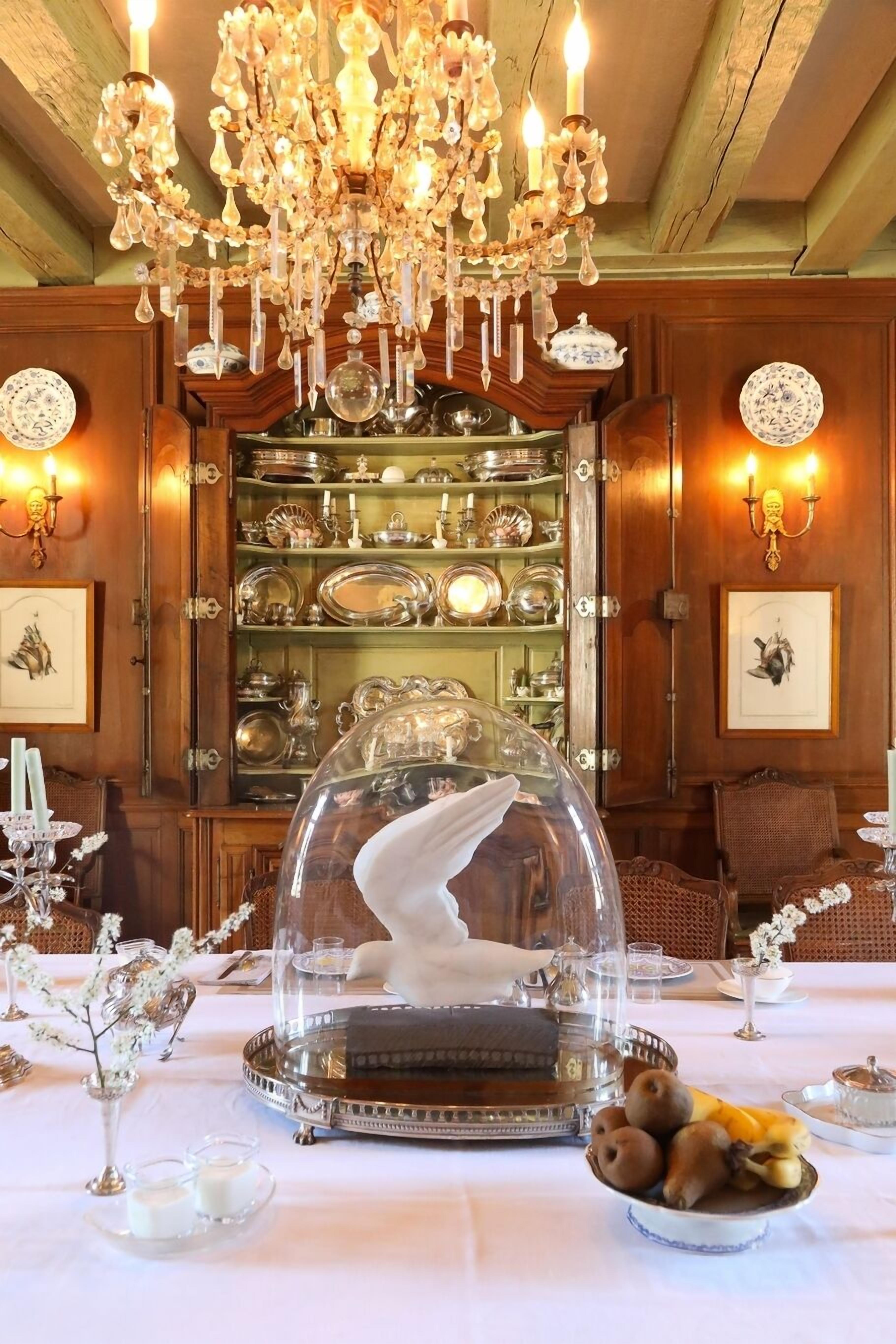A dining table with a glass dome centerpiece, surrounded by silverware and a fruit bowl.