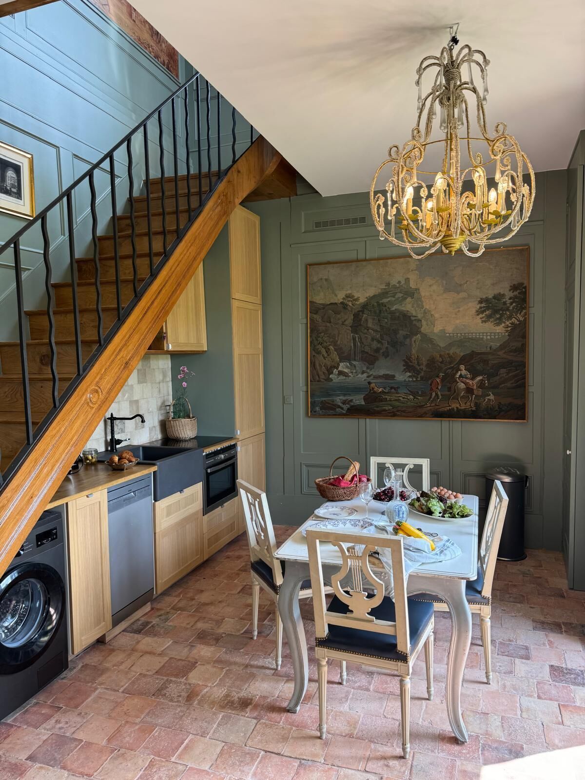 Une cuisine avec un coin repas, un escalier en bois et un lustre.
