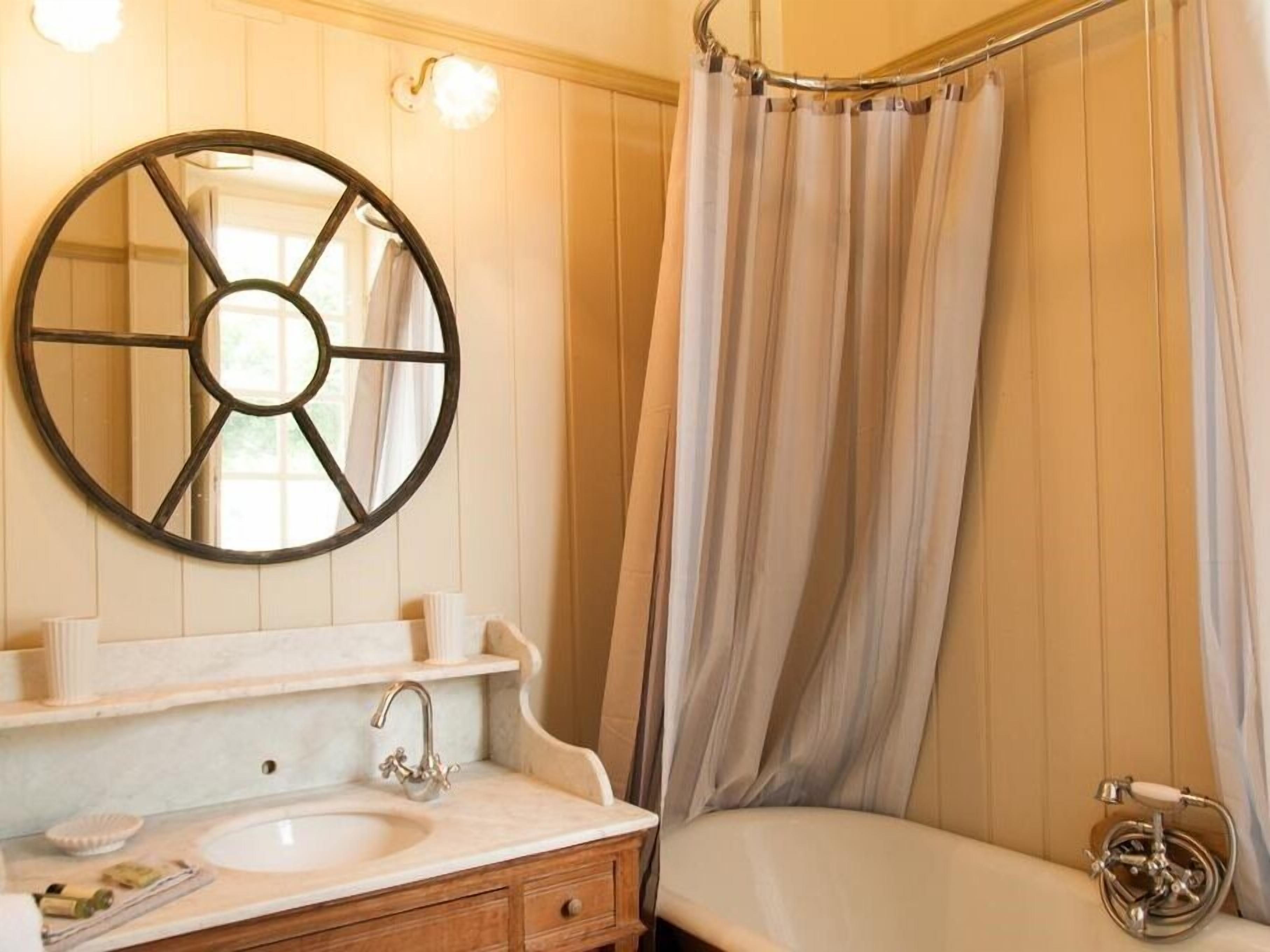 Un baño con espejo redondo, lavabo, cortina de ducha y bañera.