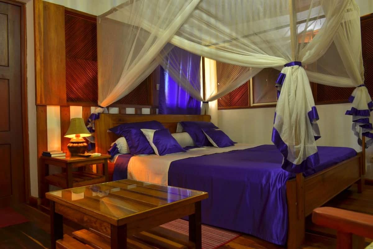 A room with a bed, a nightstand, a table, and a window with curtains.