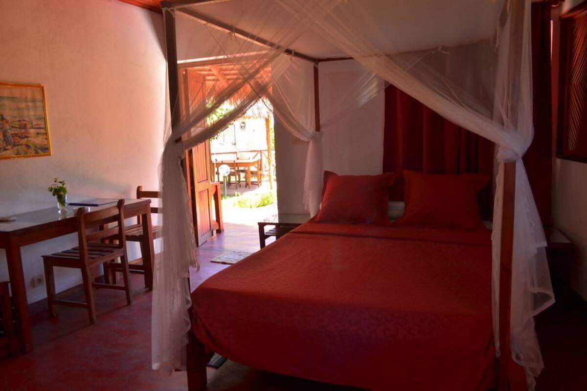 A room with a bed under a canopy, a desk with chairs, and a view of the outside.