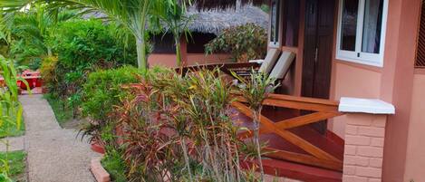 A cozy bungalow with a thatched roof, a small outdoor seating area, and lush tropical vegetation.