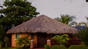 A thatched-roof building with a wooden door, surrounded by greenery and palm trees. - Edena Kely (Mahajanga)