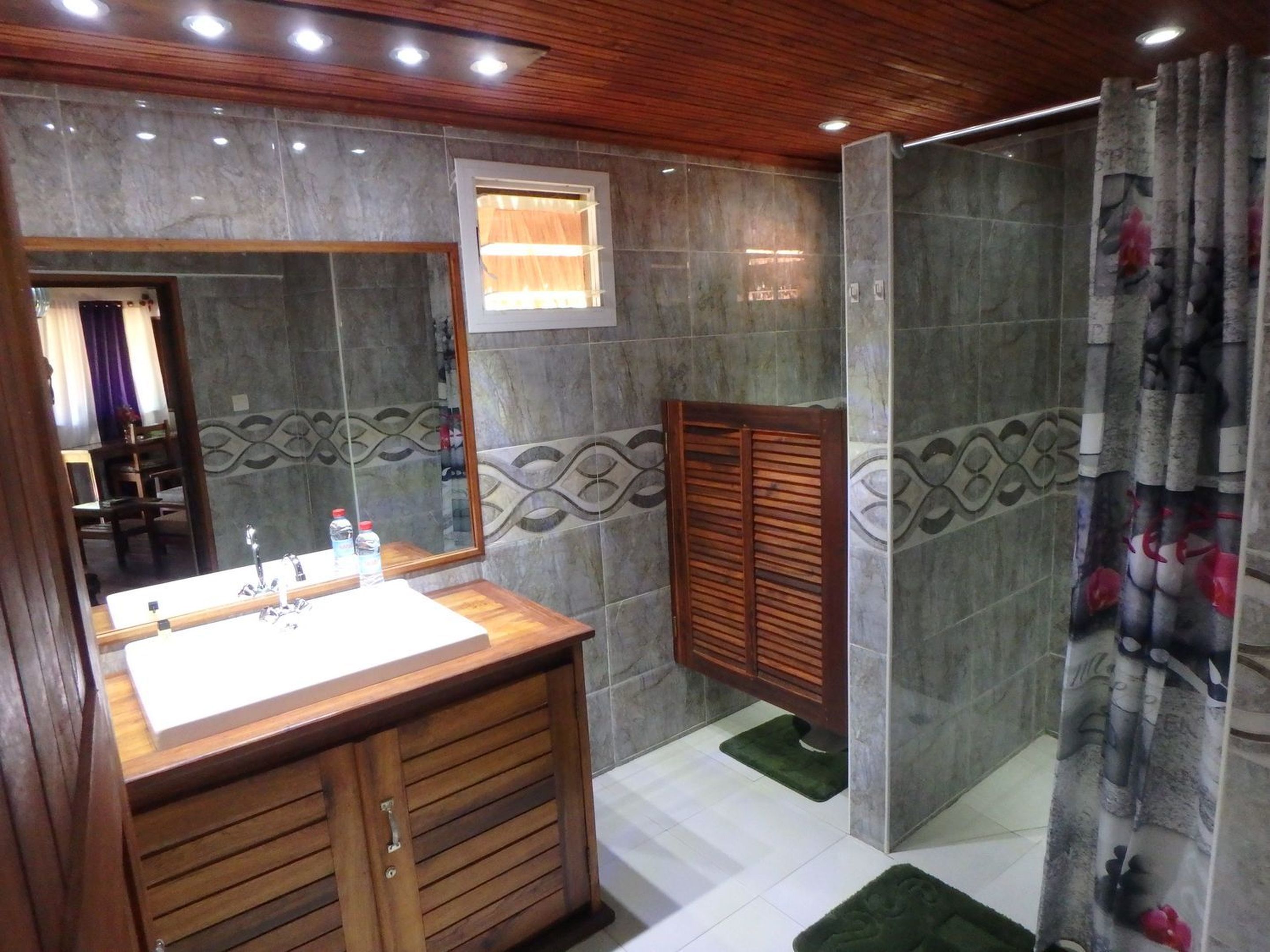 A bathroom with a wooden vanity, a shower with a curtain, and decorative wall tiles.