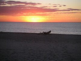 A beach scene with a boat on the sand near the water's edge during sunset.