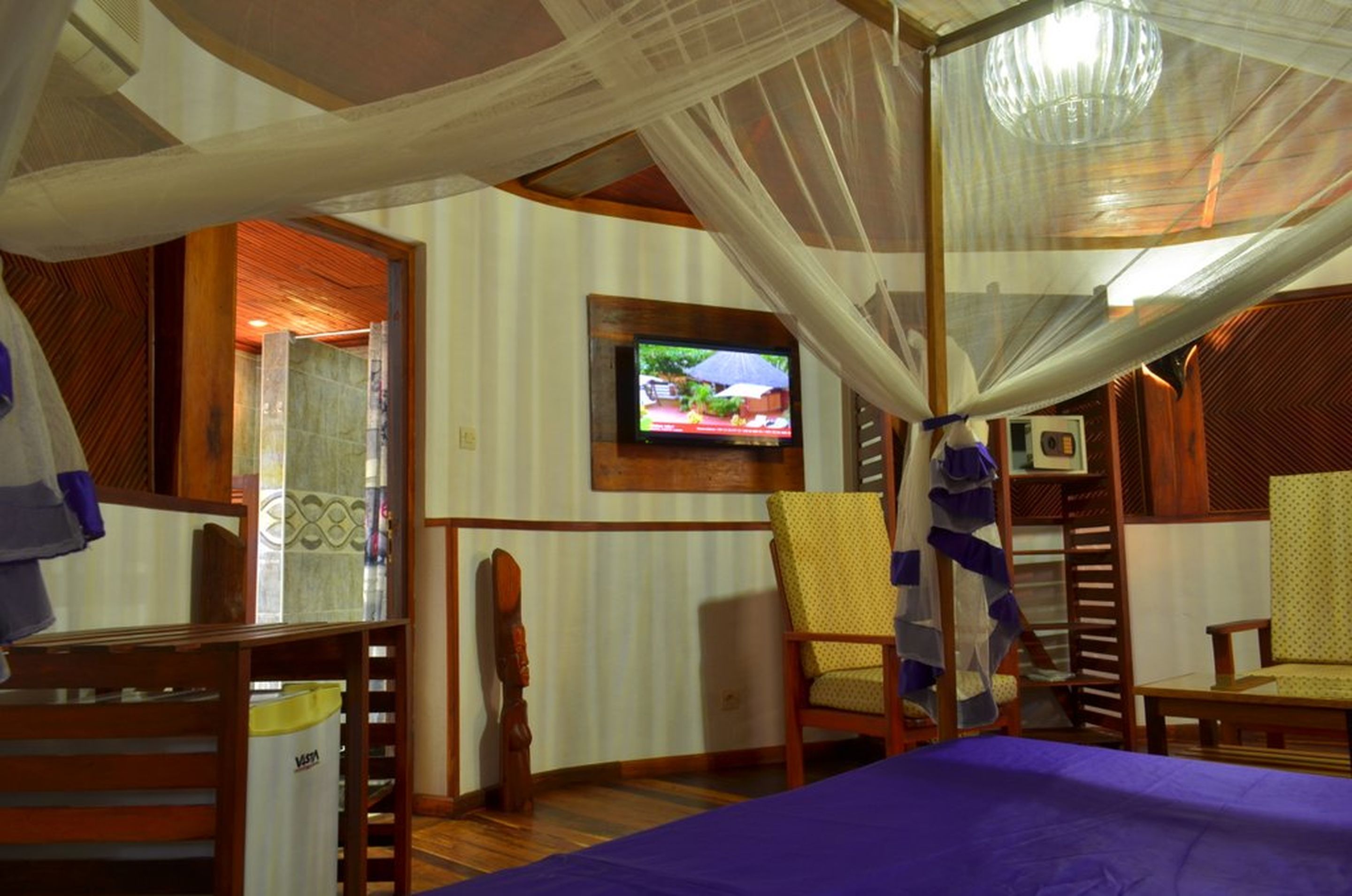 Una habitación con una cama, televisión montada en la pared y una silla.