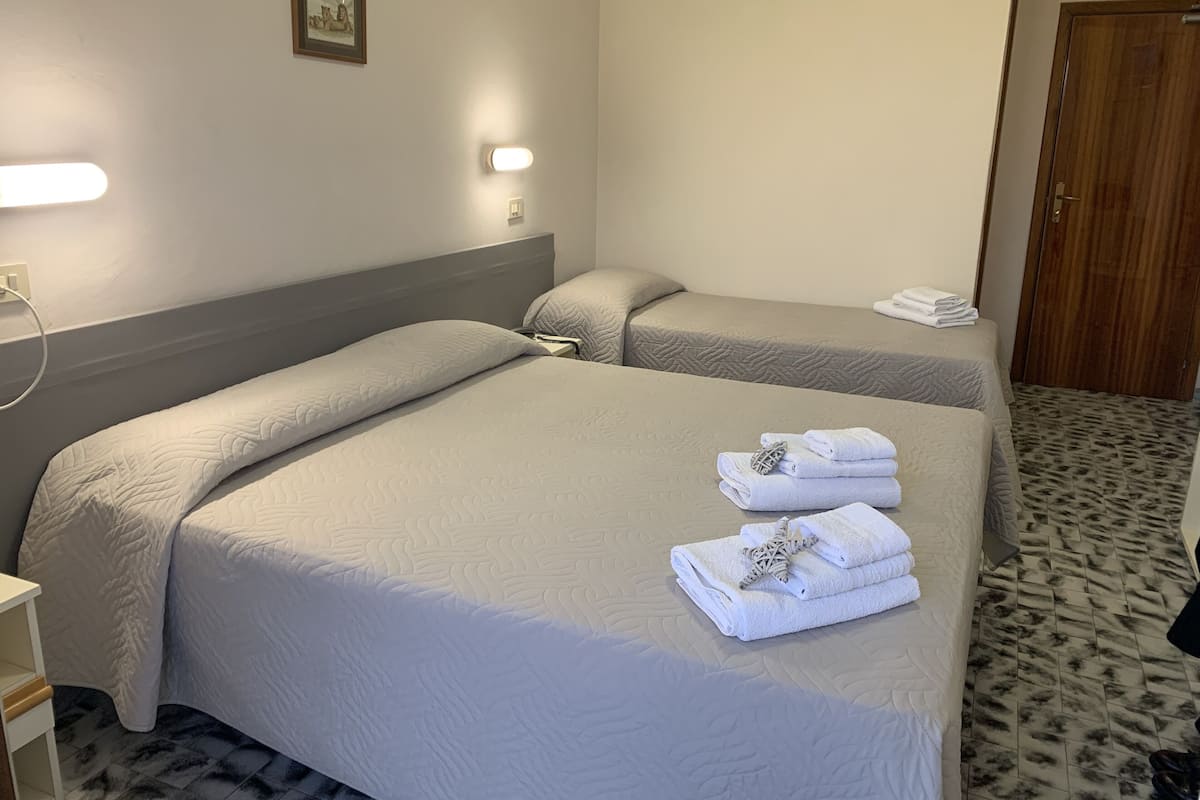 Quarto de hotel com duas camas, uma mesa de cabeceira, um abajur e uma porta.