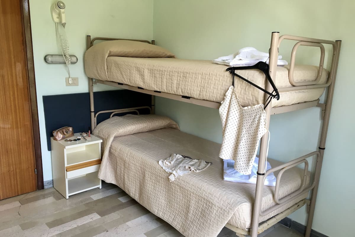 Quarto com beliche, mesa de cabeceira, cabideiro e telefone fixo na parede.