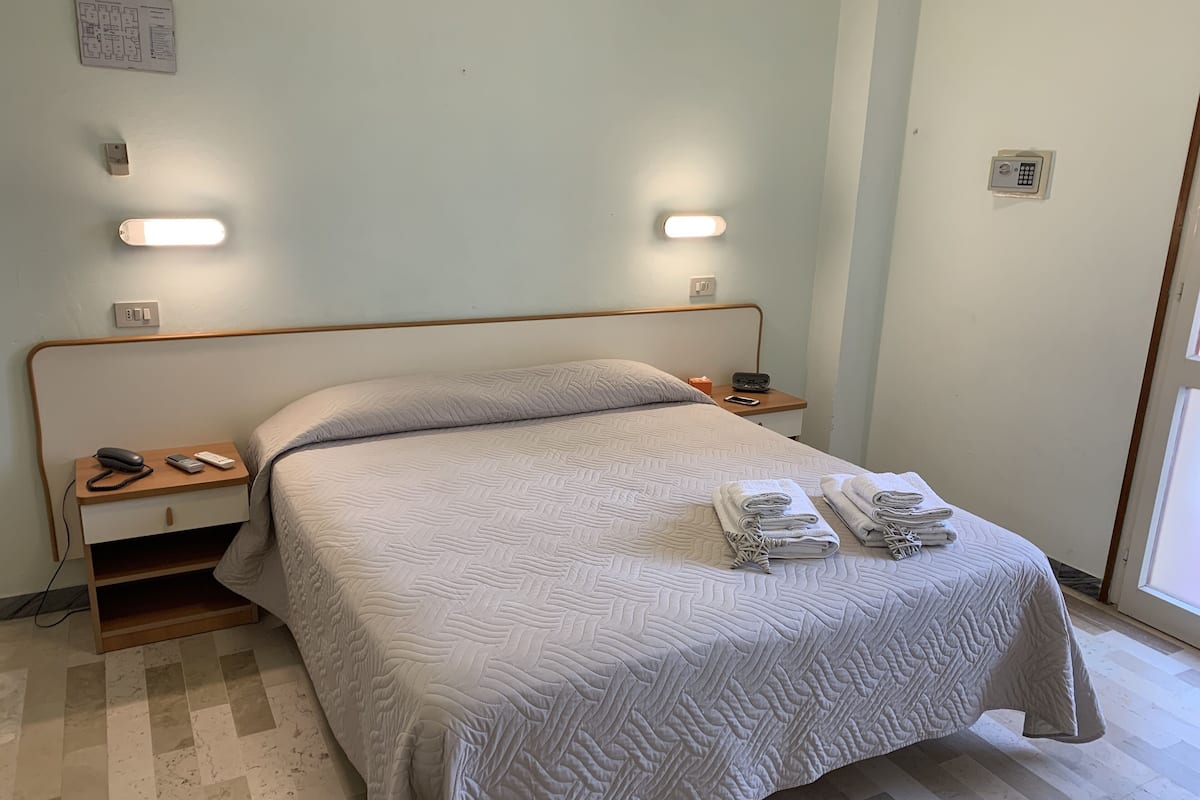 Uma cama bem arrumada com um edredom estampado, mesas de cabeceira com abajures, um telefone e um rádio.