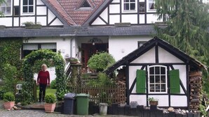 A traditional half-timbered house with a sloped roof, a front porch, and a small garden area with potted plants and a wooden fence. - Landhaus Lichthof (Lohmar)