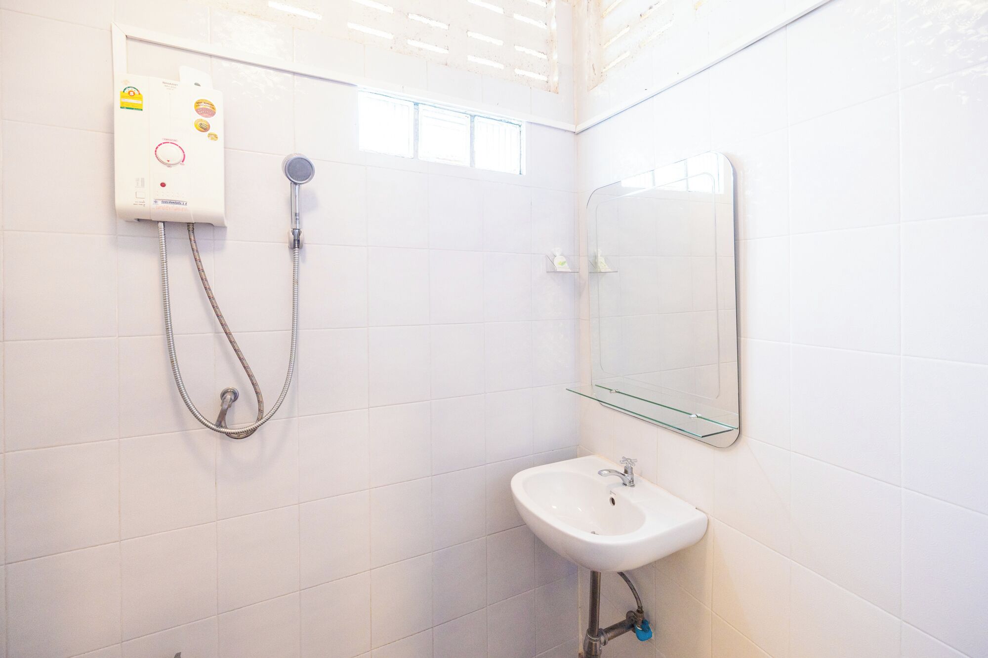 A bathroom with white tiled walls, a glass shower enclosure, a white sink, and a mirror.