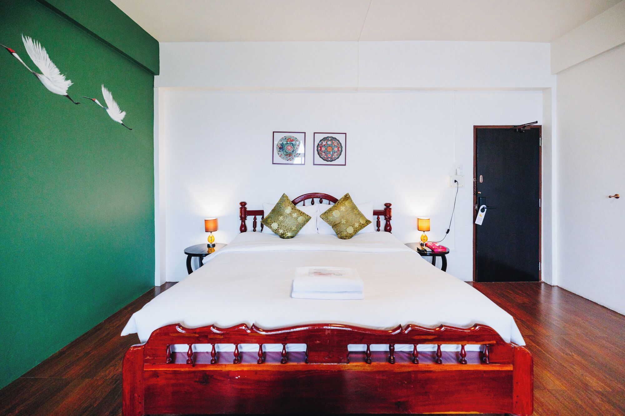 A hotel room with a wooden bed, two bedside tables with lamps, a green accent wall, and two decorative plates on the wall.