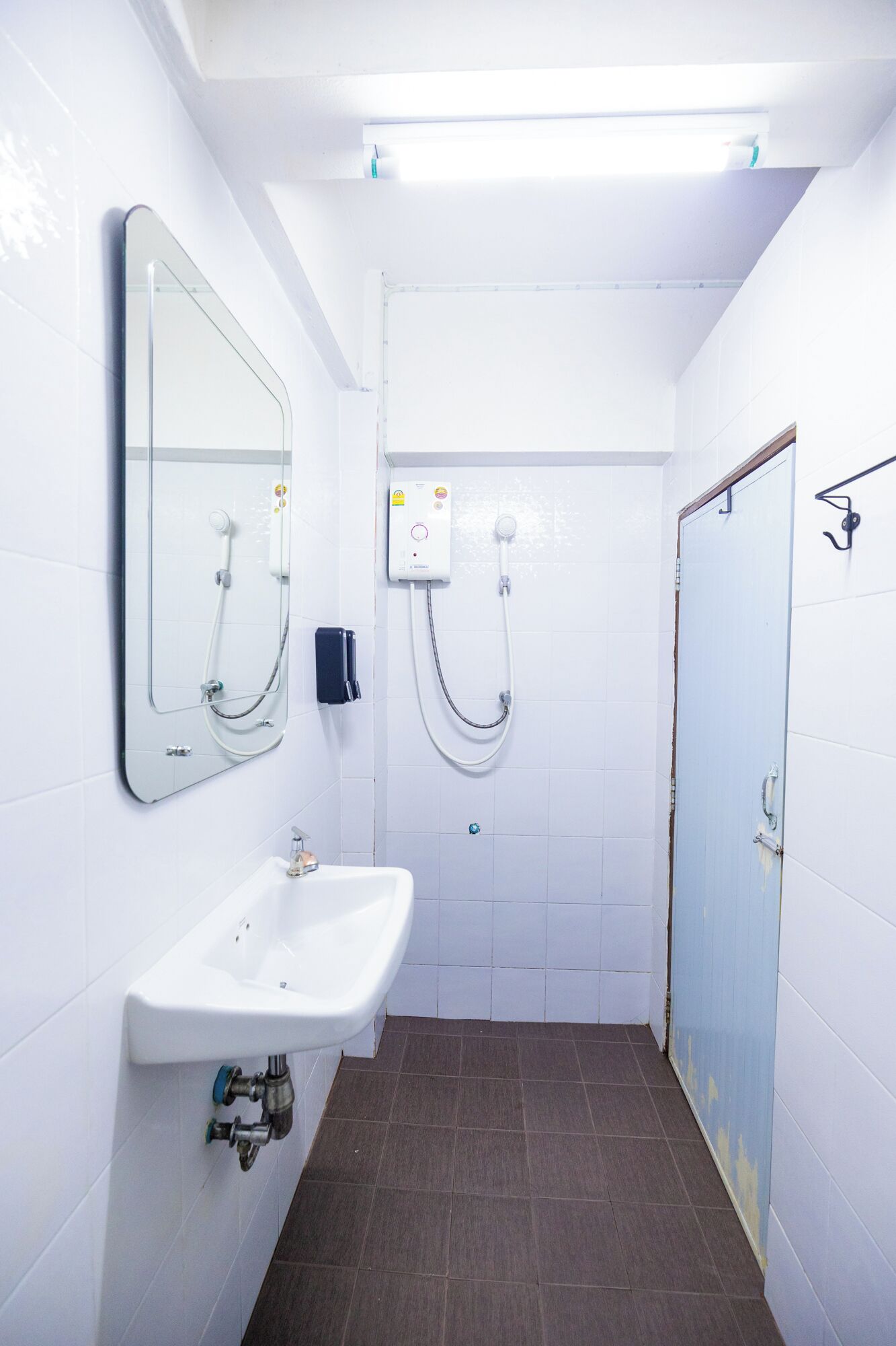 A small, white bathroom with a sink, mirror, and shower.
