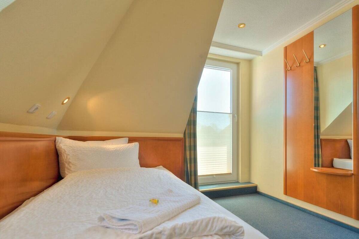 Habitación de hotel con cama, armario de madera, ventana y espejo.