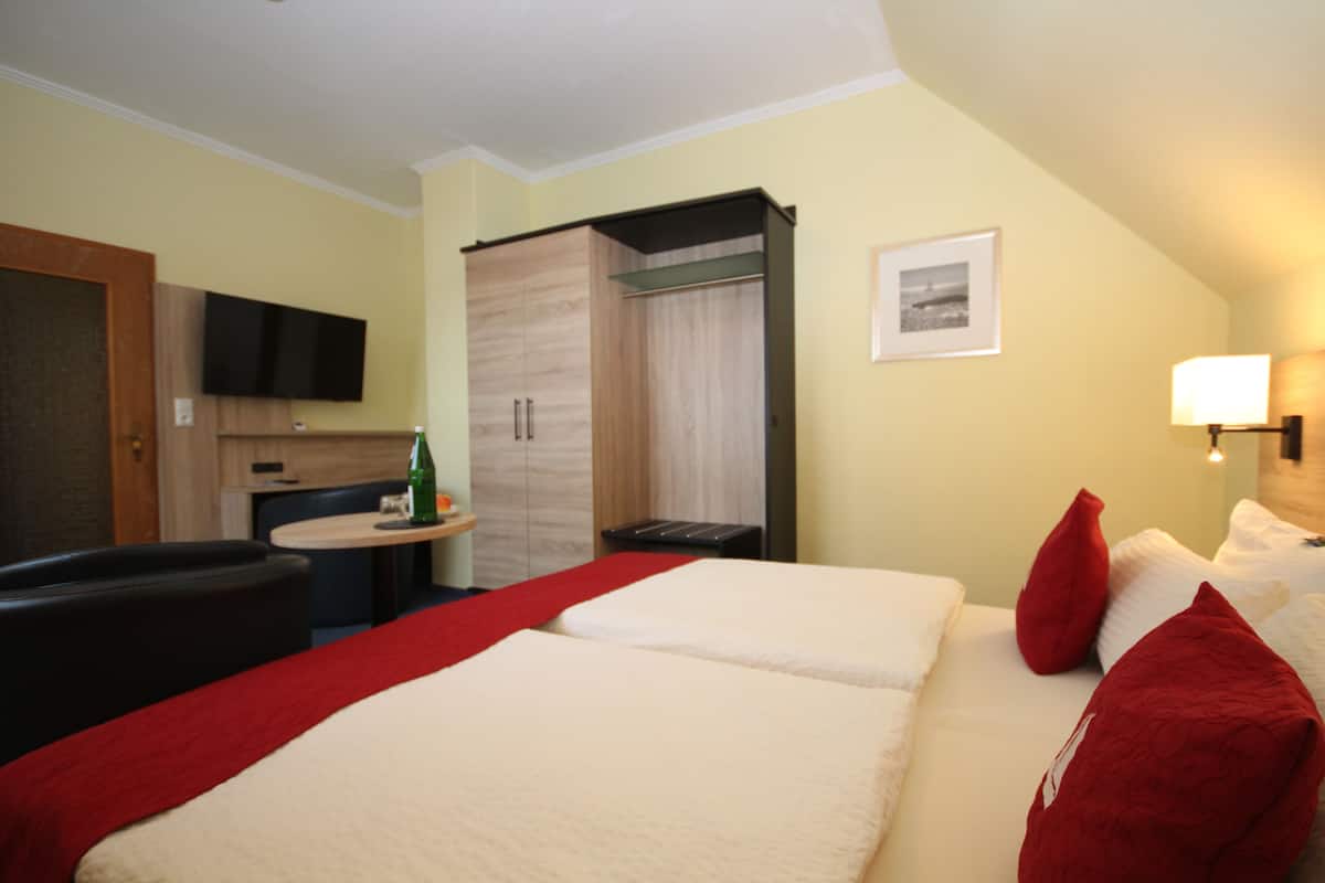 Una habitación de hotel con dos camas, televisión, una mesita con una botella y un armario.