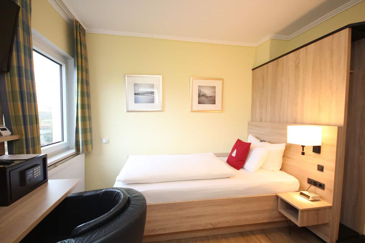 Una habitación de hotel con una cama, mesita de noche, lámpara y microondas en una encimera.