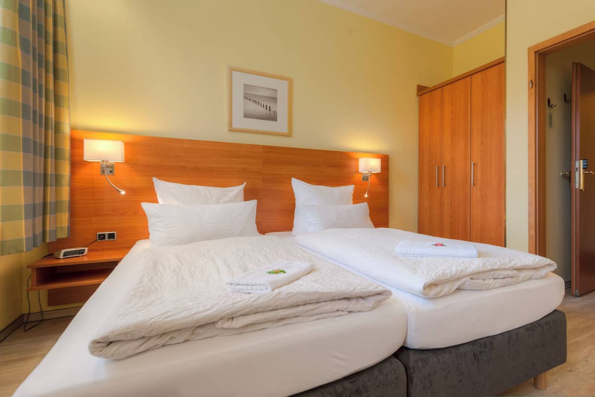 Habitación de hotel con dos camas, cabecero de madera, lámparas de noche, mesitas de noche, un cuadro colgado en la pared y un armario.