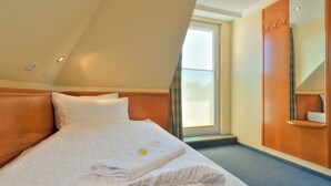 Una habitación de hotel con cama, armario de madera, ventana con persianas y un pequeño balcón.