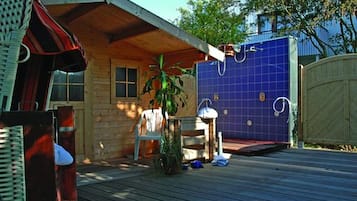 A wooden cabin with a patio, a blue hot tub, and a small table with a plant.