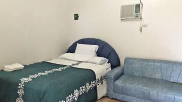 A bedroom with a bed, a blue sofa, a wall-mounted air conditioner, and a small green device on the wall.