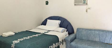 Un dormitorio con una cama, un sofá azul, un aire acondicionado instalado en la pared y un pequeño dispositivo verde en la pared.