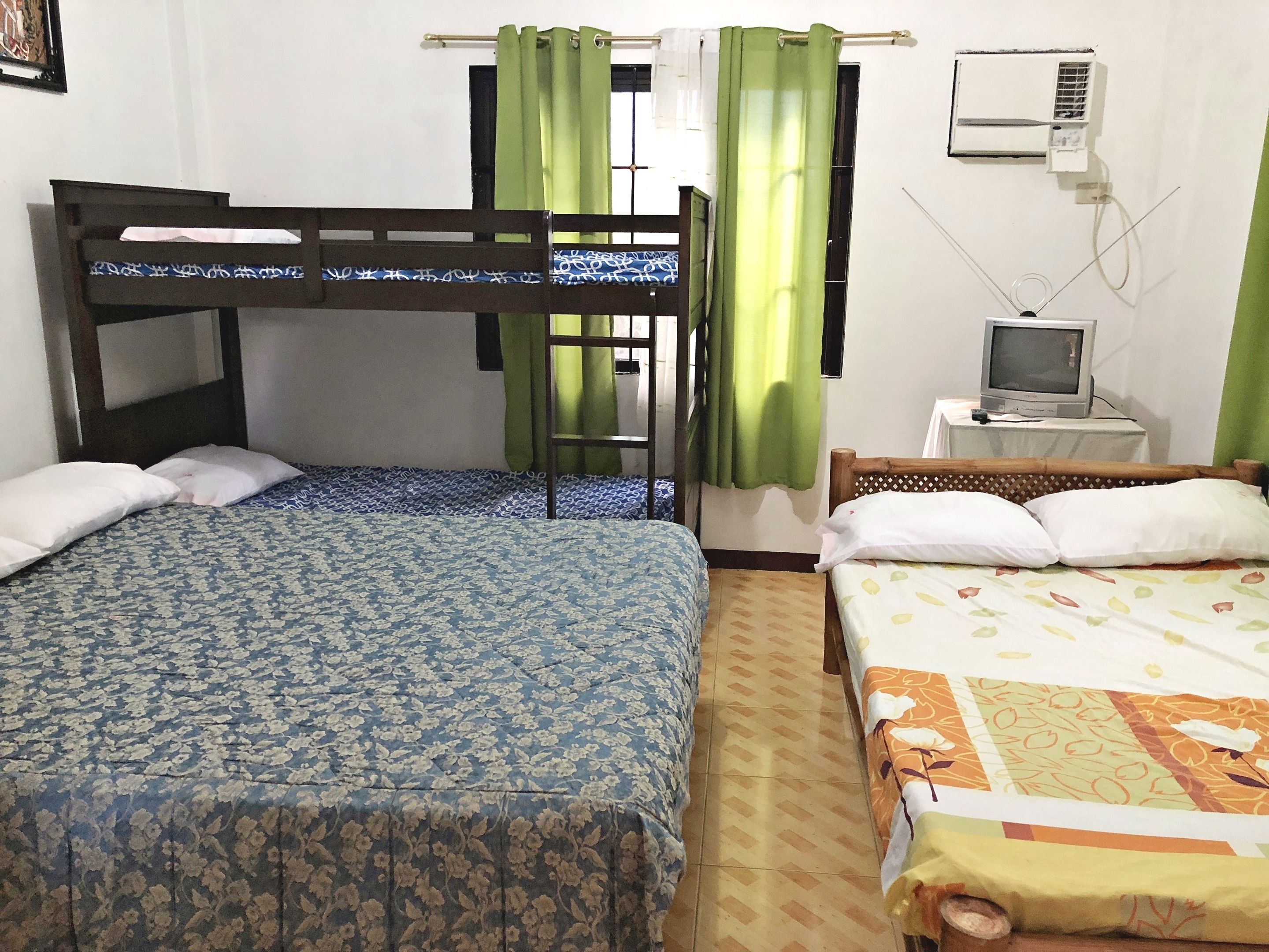 A room with two beds, a television, and a window with curtains.