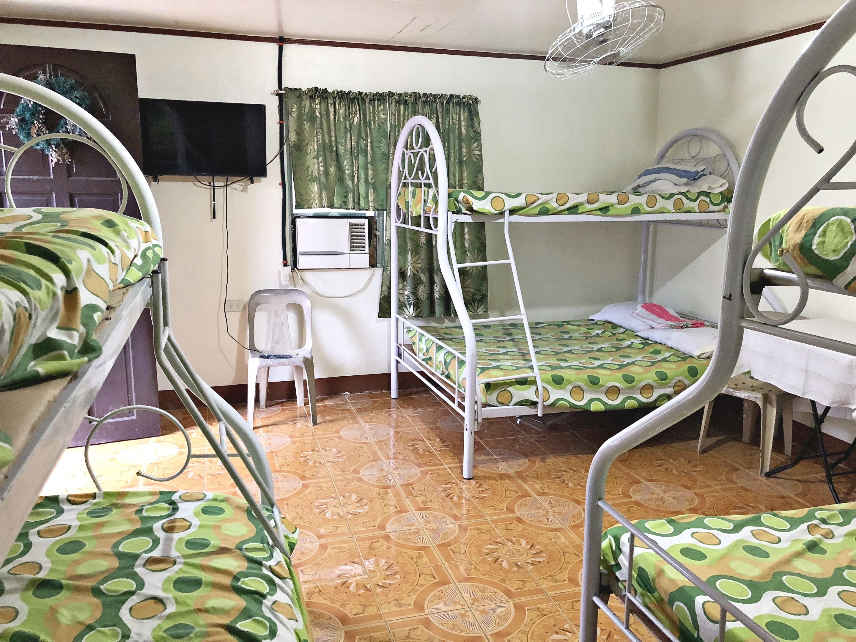 Une chambre de dortoir équipée de lits superposés, d’un téléviseur, d’un climatiseur et d’un ventilateur.