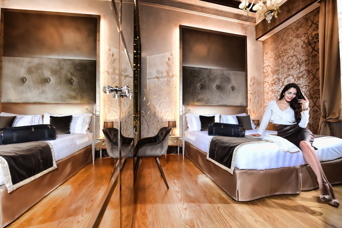 Une chambre d’hôtel avec deux lits, un coin salon avec un fauteuil et un grand miroir.
