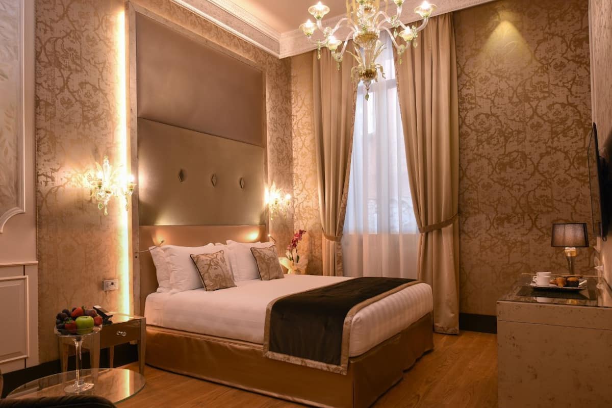 Une chambre d’hôtel avec un grand lit, un lustre, un bureau avec une lampe et une télévision.